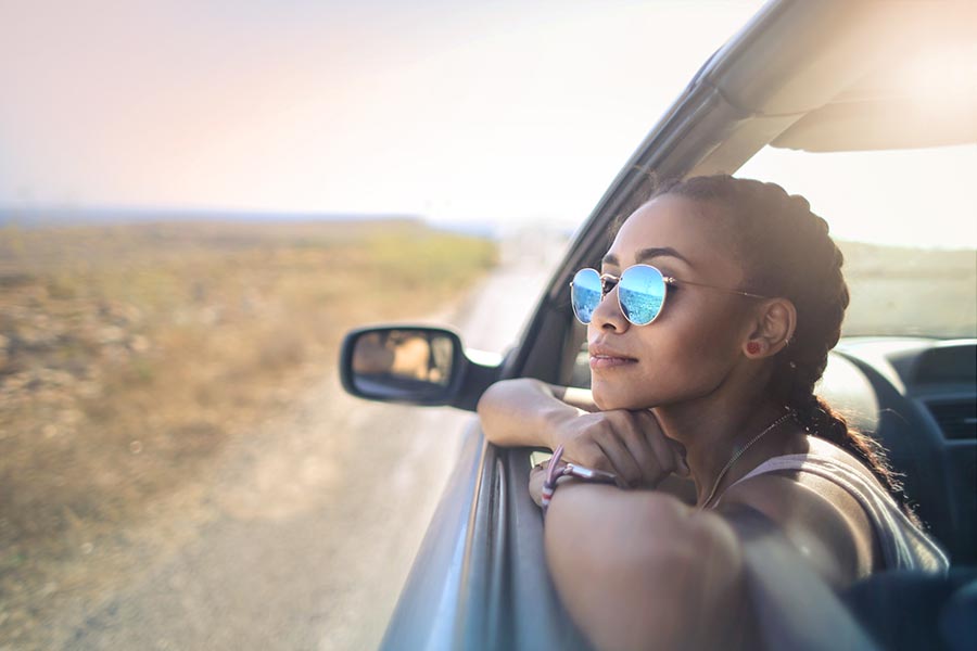 About Our Agency - Young Woman Looks Out the Window of a Car Driving Through the Southwest United States, the Blue Sky Reflected in Her Glasses