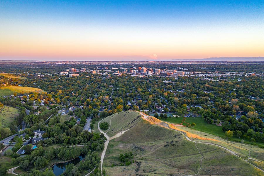 Boise, ID Insurance - Aerial Shot of Boise, Idaho From a Distance, With Green Hills in the Foreground and the Skyline Glowing Pink in the Sunset