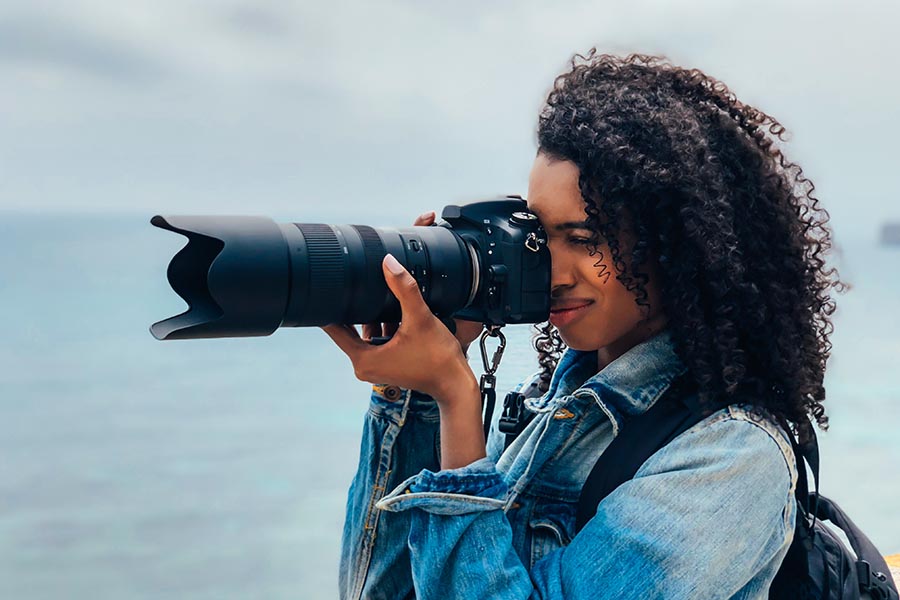 Specialized Business Insurance - Photographer Uses Large Professional Camera Standing by the Ocean Wearing a Jean Jacket